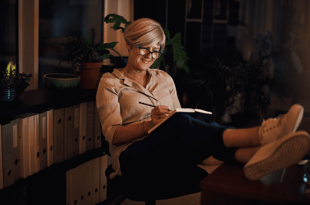 A woman smiling as she writes her memoir by hand in a notebook