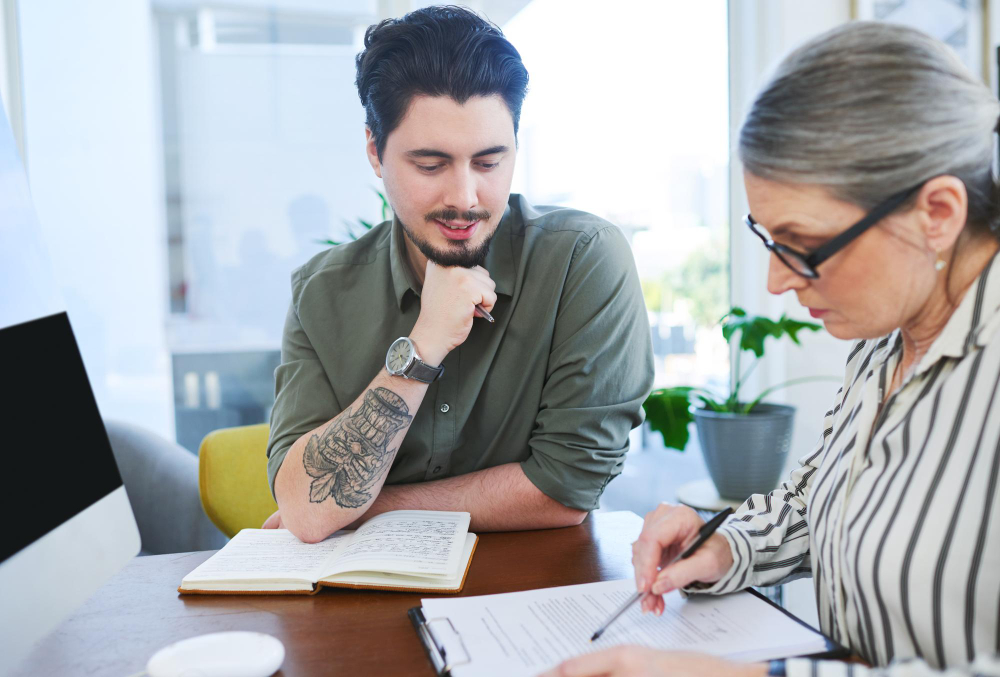 A memoir editor and a writer working through manuscript pages together with pens and notebooks